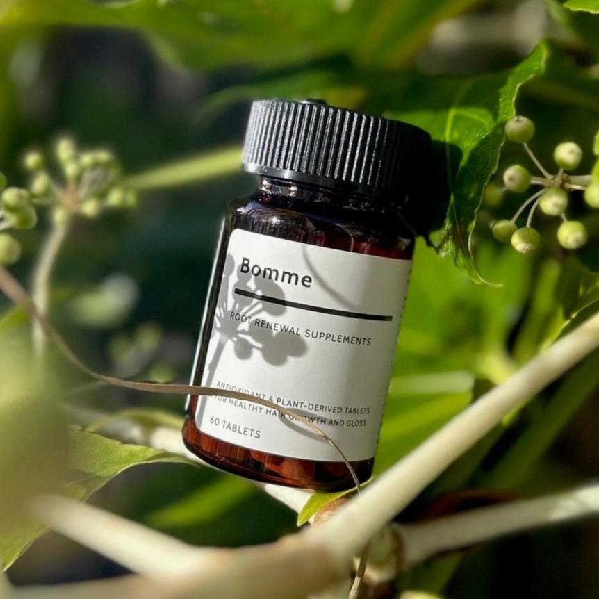 Bomme Root Renewal Supplements bottle nestled among green leaves and plant stems, with natural sunlight casting shadows across the label, emphasizing natural ingredients.