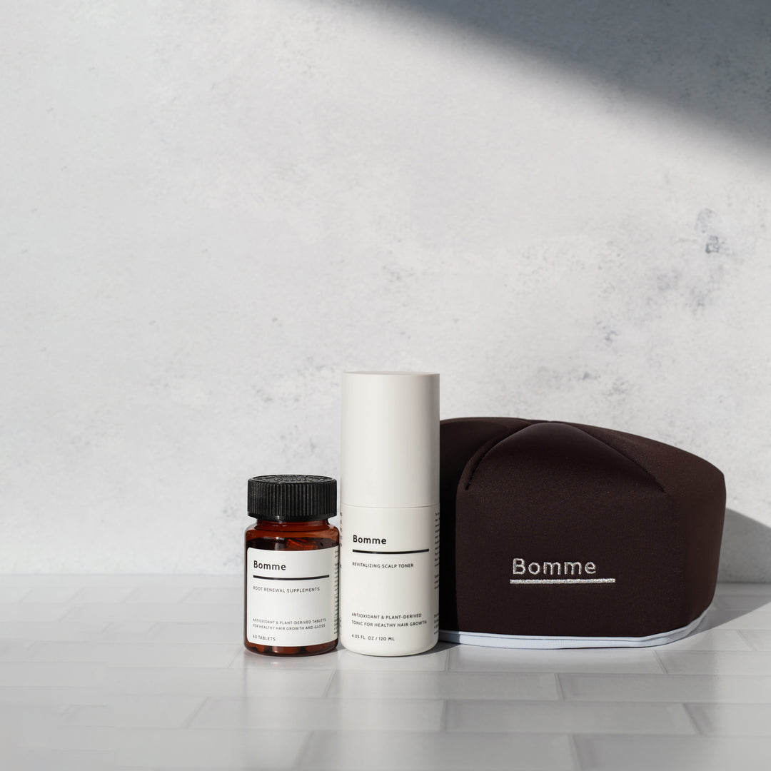 Bomme hair care set with supplements, scalp toner, and LED red light cap on a tiled surface with soft shadows