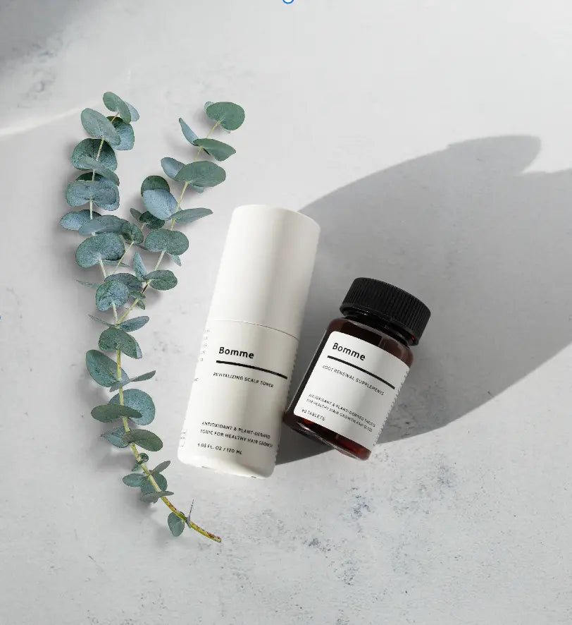 Two Bomme haircare products with eucalyptus leaves on a light surface