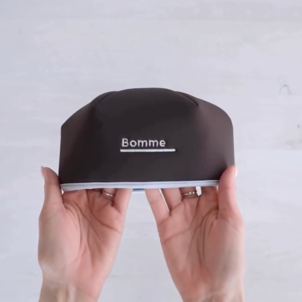 Hands holding the Bomme LED Red Light Scalp Device, demonstrating lightweight design and premium construction.