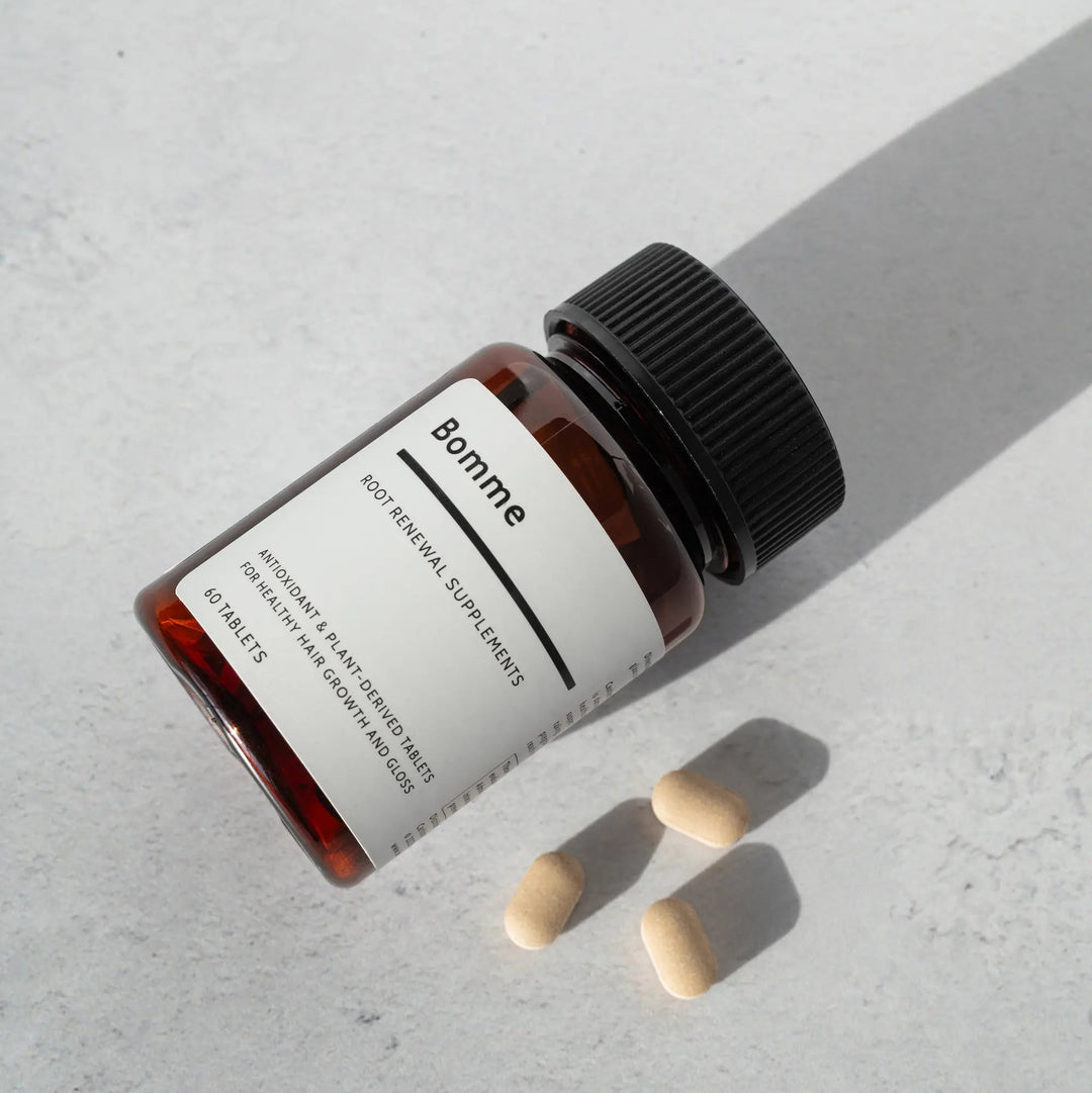 Bottle of Bomme supplements on a light gray surface with three tablets beside it.