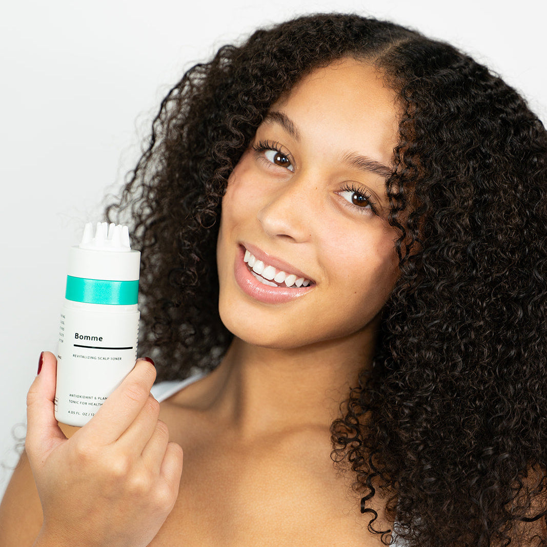 Woman holding a bottle of Bomme Scalp Toner against a white background