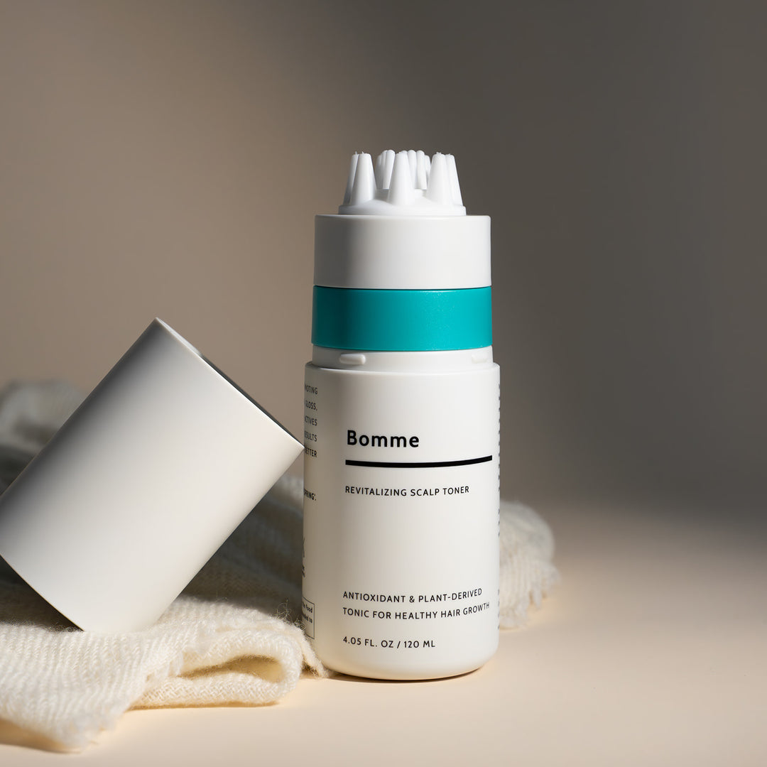 Bomme revitalizing scalp toner bottle with a white cap on a beige surface.