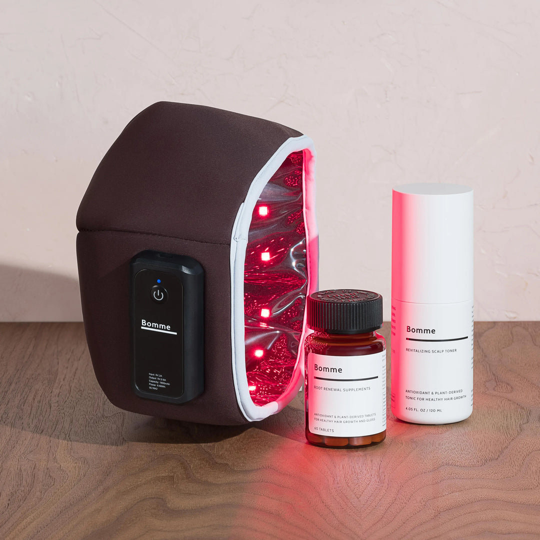 Bomme LED Red Light Device with the red lights on with Root Renewal Supplements and Bomme Scalp Toner bottles next to it