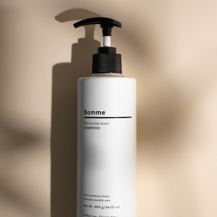 Bomme Revitalizing Scalp Shampoo standing upright on a beige background with soft lighting.