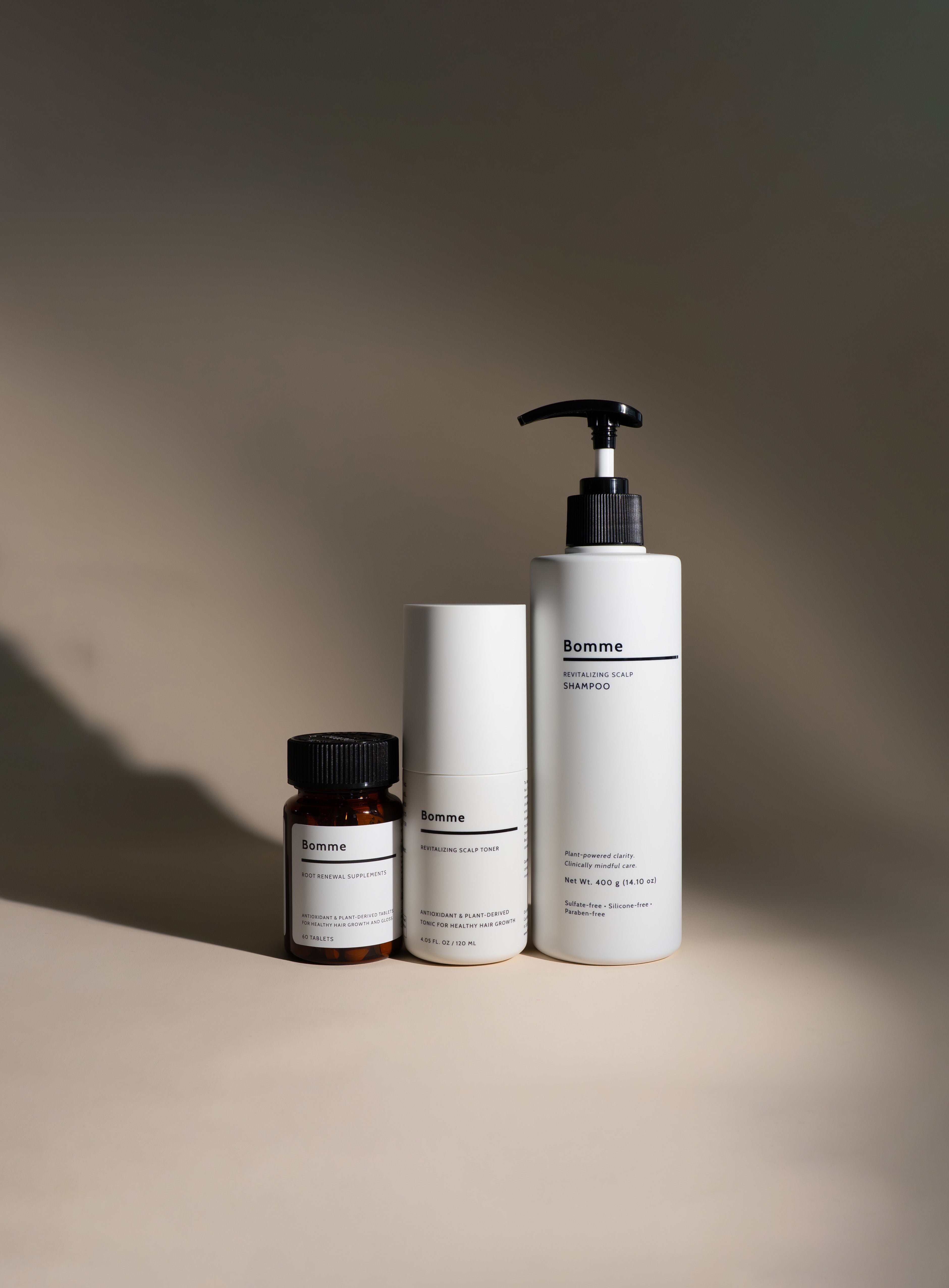 Bomme hair-care trio: Root Renewal Supplements, Revitalizing Scalp Toner, and Revitalizing Scalp Shampoo on a beige background with soft shadow.