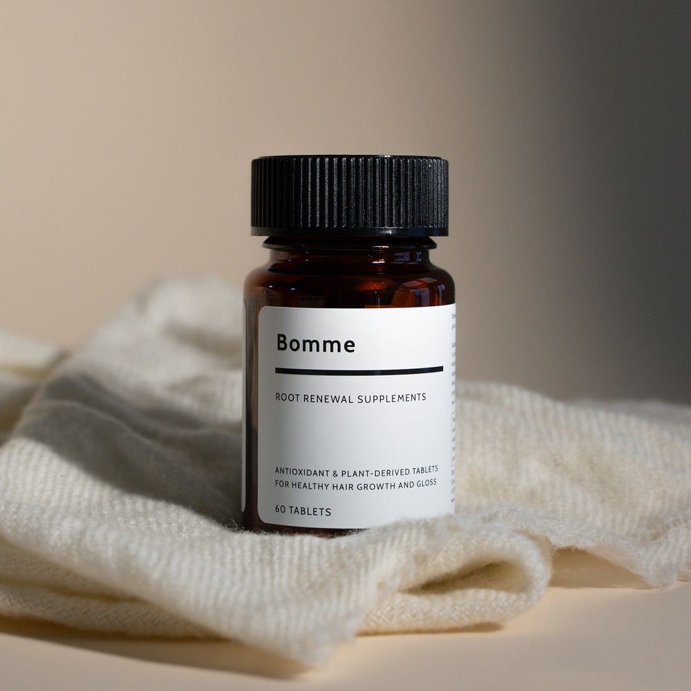 Bomme Root Renewal Supplements bottle on soft folded cloth, photographed in natural light for lifestyle look.