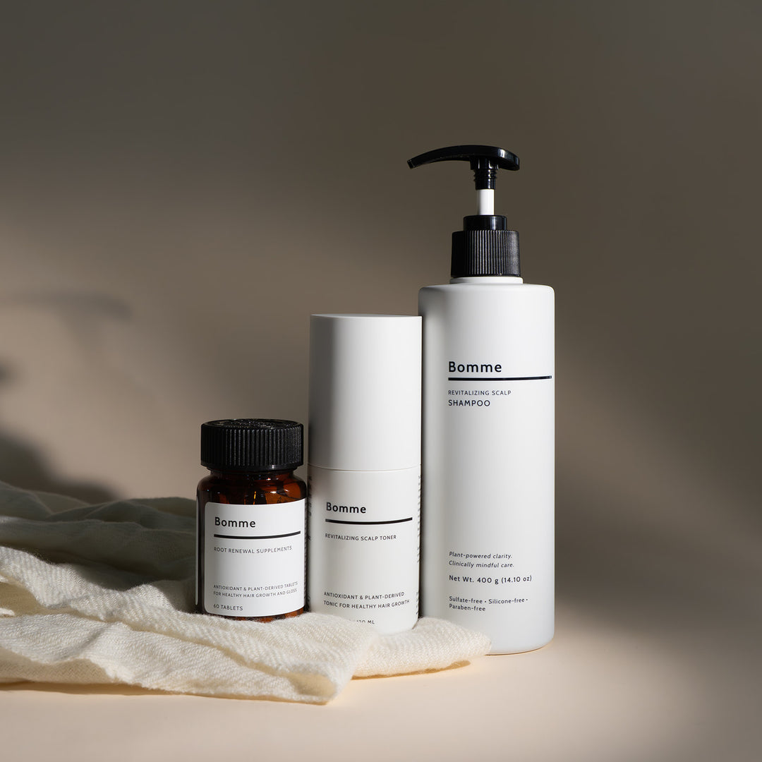 The Bomme Ritual 3-step hair wellness system with supplement, toner, and shampoo on a soft neutral fabric.”