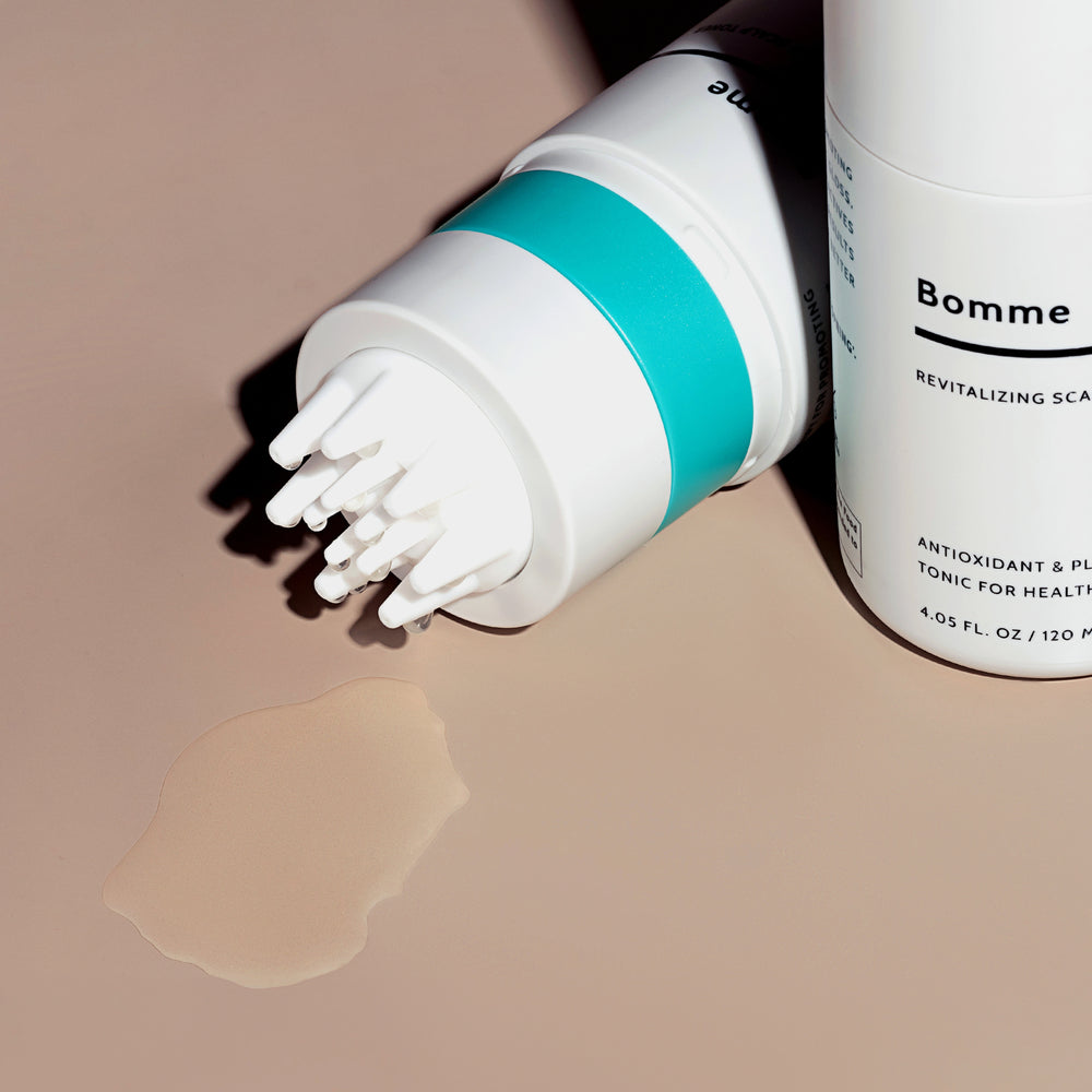 Revitalizing Scalp Toner bottle tipped with product spilled beside it. Clear liquid texture shown on beige surface.