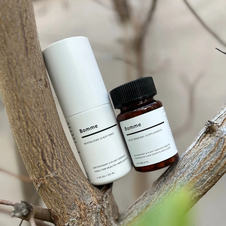Bomme Root Renewal Supplement and Revitalizing Scalp Toner styled naturally among tree branches.